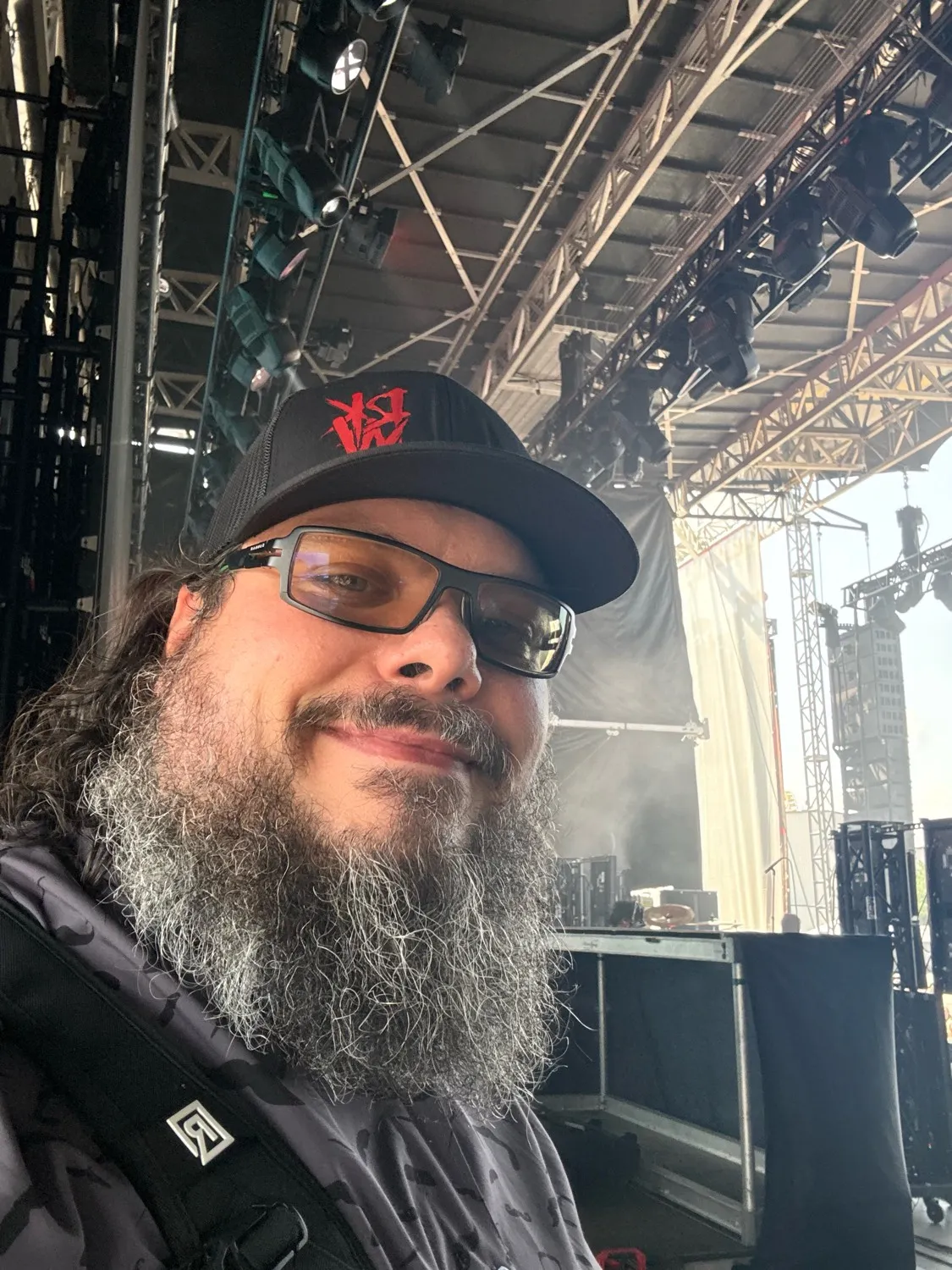 Self-portrait of Zach Stepek on location at an outdoor stage, lighting truss and rigging visible behind.