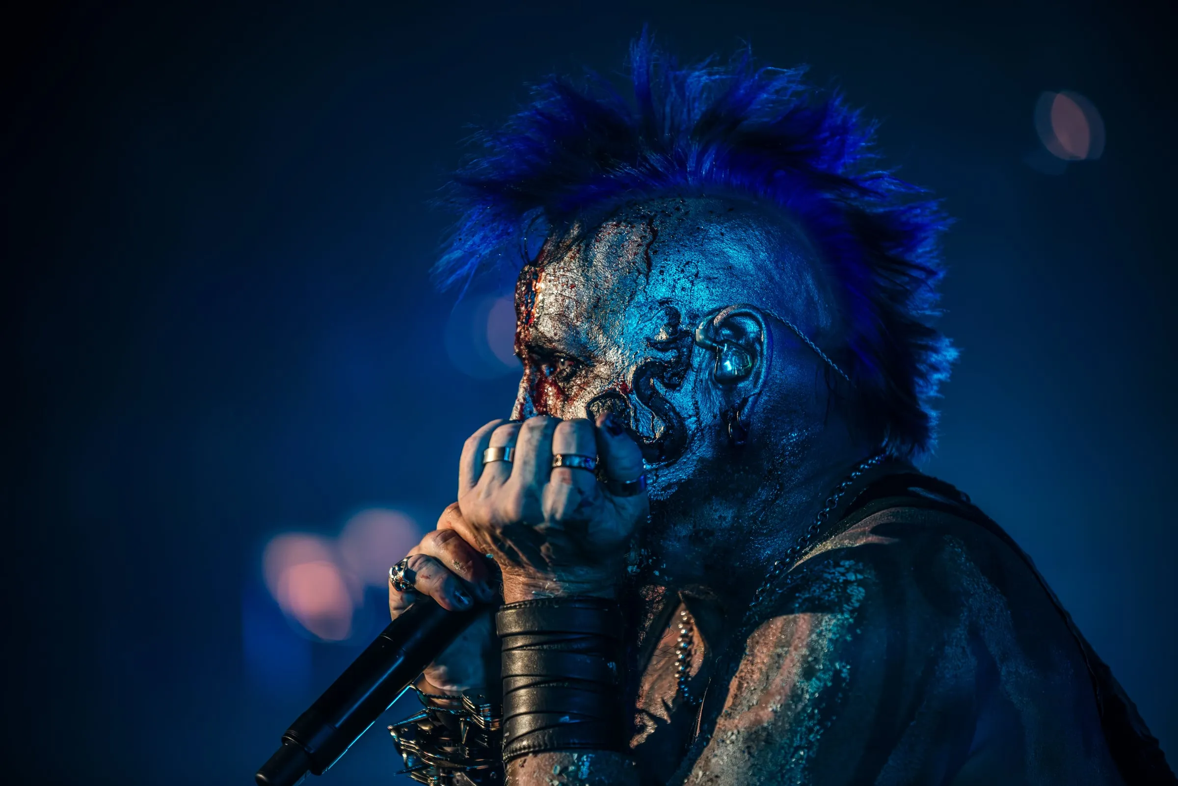 Chad Gray of Mudvayne in stage face paint and blue mohawk, holding the microphone close to his mouth under deep teal stage light at The Rave, Milwaukee, 14 July 2022.