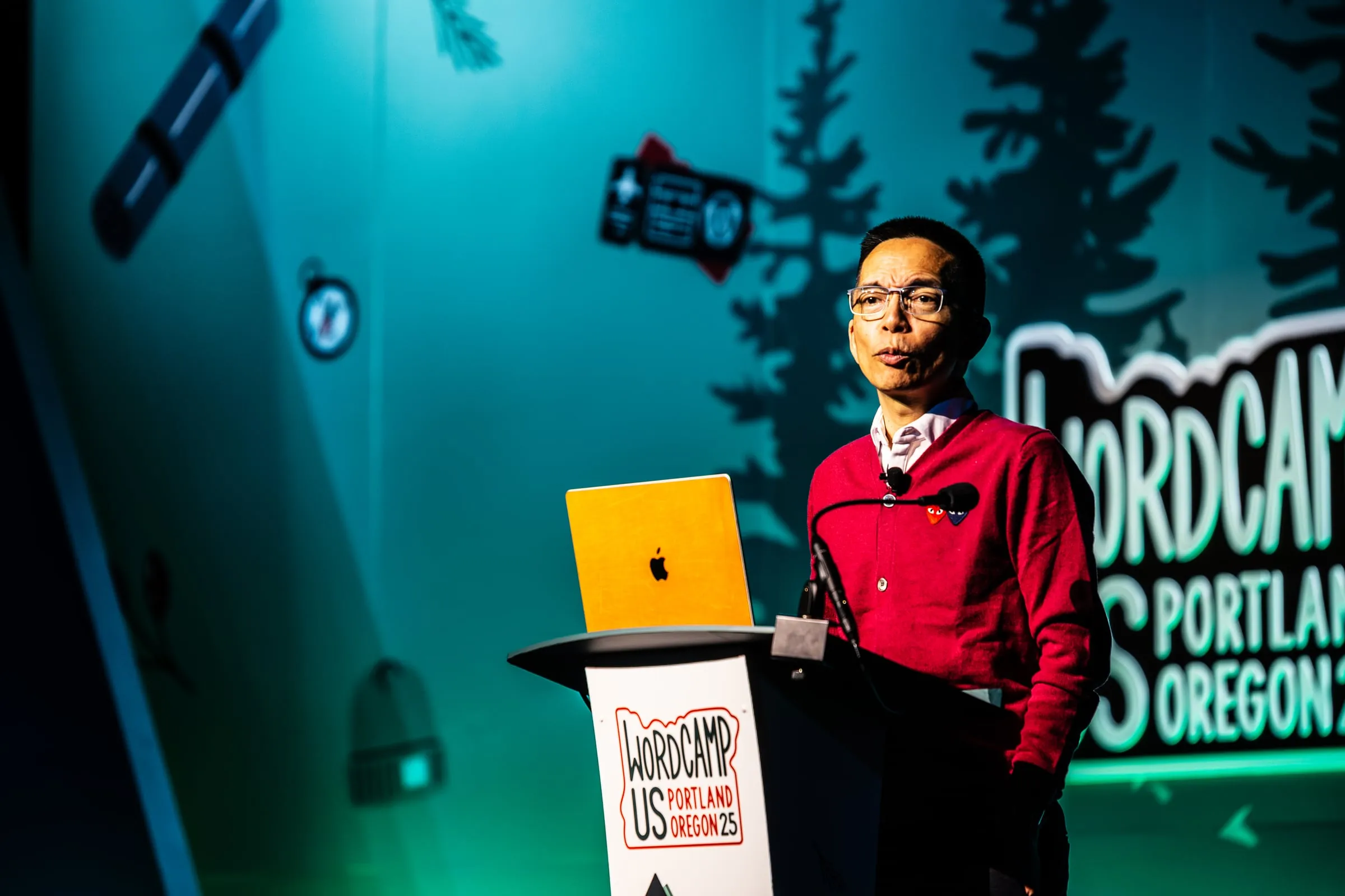 John Maeda delivering a WordCamp US 2025 keynote in a red sweater on the Portland conference stage.